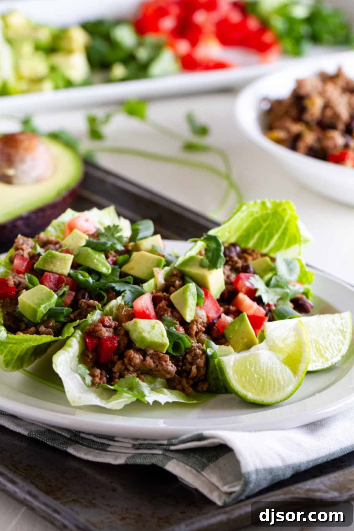 Two taco lettuce wraps on a plate, topped with tomatoes, avocado, and lime juice.