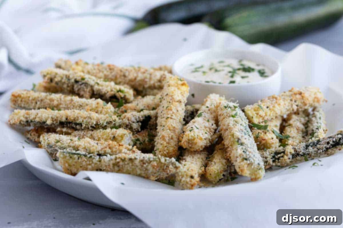 A vibrant plate filled with golden-brown baked zucchini fries, ready to be dipped into a creamy sauce.