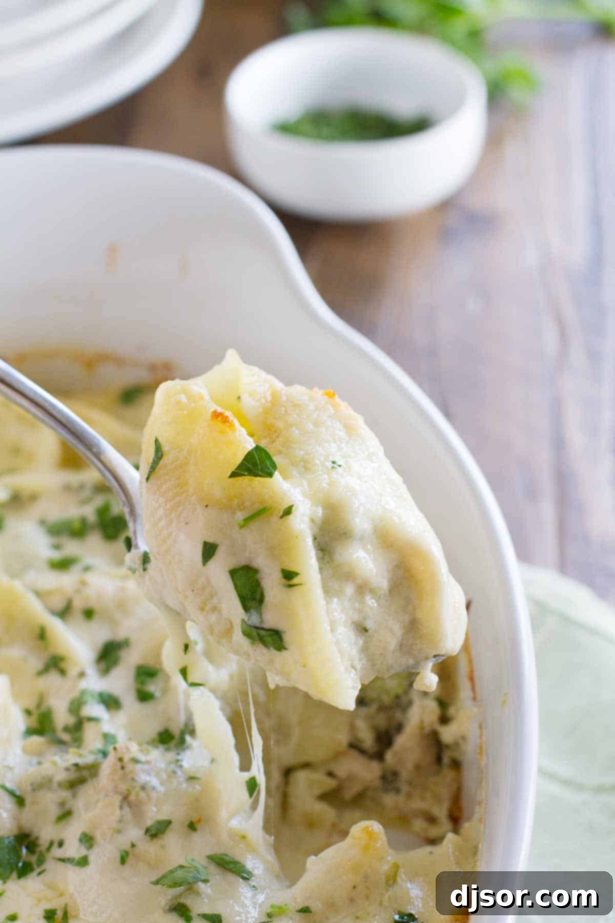 Creamy Chicken Alfredo Stuffed Shells spooning out a stuffed shell from the baking dish, showing the creamy filling