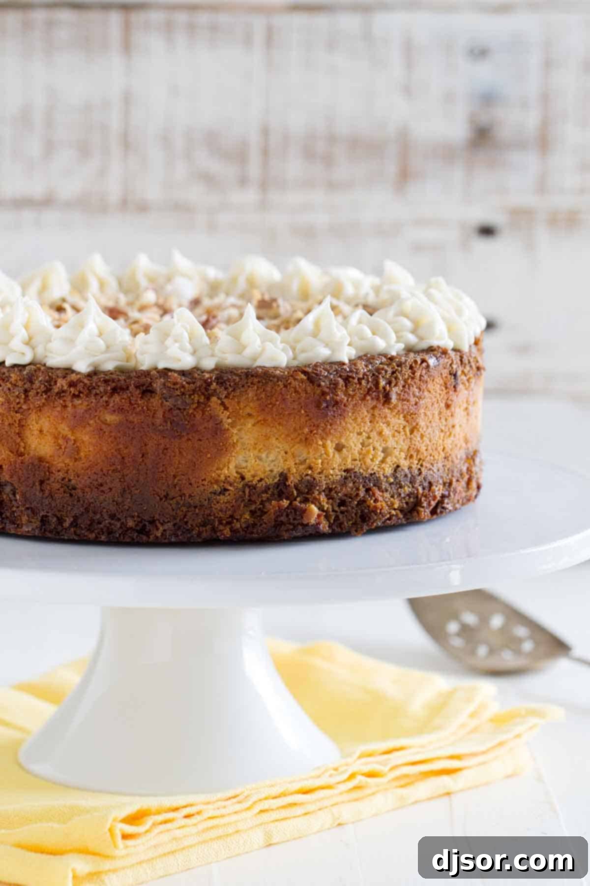 Indulge in the luscious layers of our Carrot Cake Cheesecake, a perfect blend of fluffy cake and creamy cheesecake, topped with a rich cream cheese frosting and crunchy pecans. A complete Carrot Cake Cheesecake, beautifully frosted and garnished with toasted coconut and pecans, presented on a elegant cake stand. Ideal for any celebration, this dessert is a harmonious blend of classic flavors.