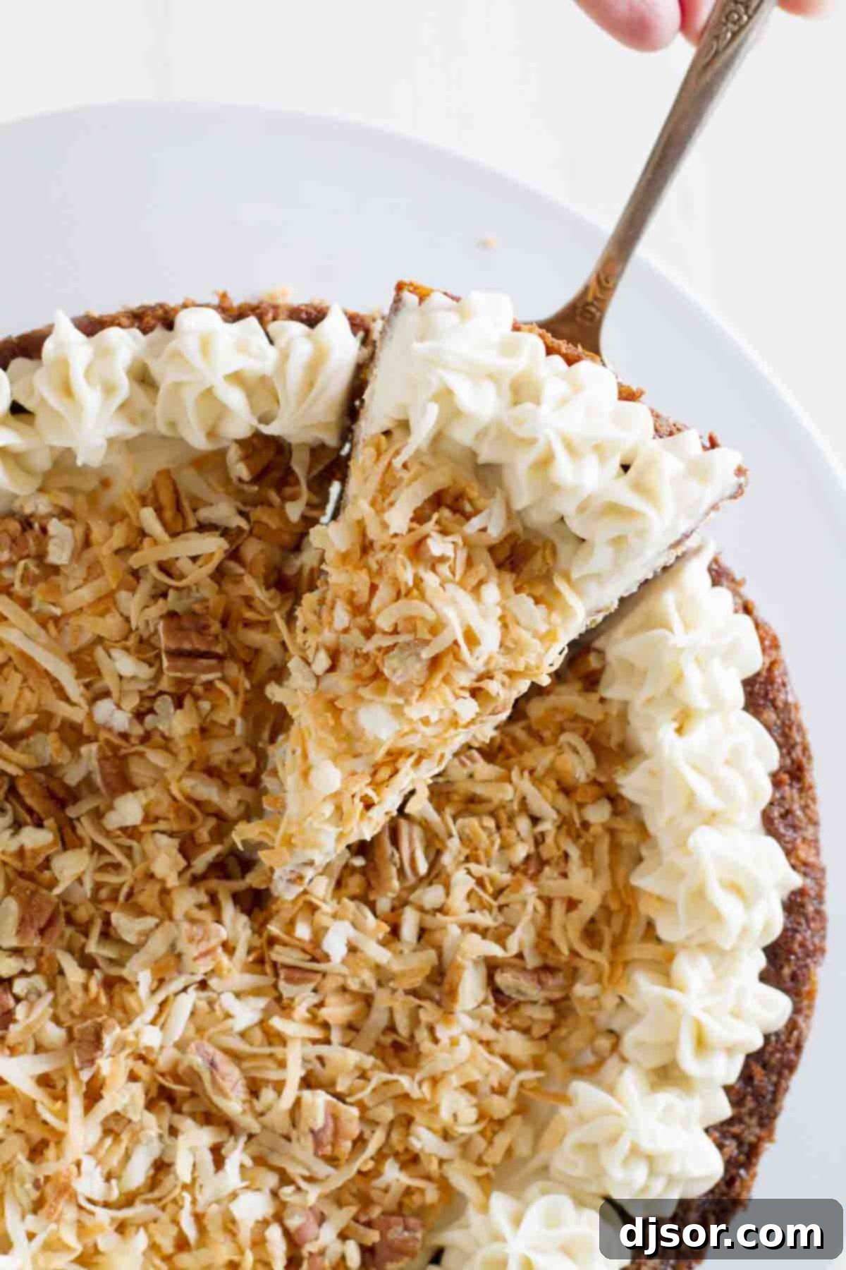 Capture the moment: a slice of heavenly Carrot Cake Cheesecake is lifted, showcasing its enticing layers and the promise of a delightful dessert experience. An overhead shot of a hand gently taking a slice of Carrot Cake Cheesecake from the pan, revealing its beautifully baked layers of carrot cake and cinnamon cheesecake, ready to be enjoyed.