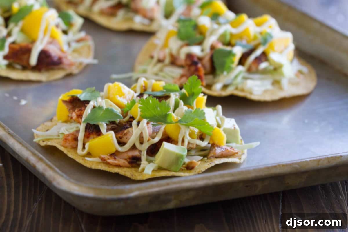 Blackened Salmon Tostadas topped with a creamy sauce, mango, avocado, and cilantro, presented artfully.