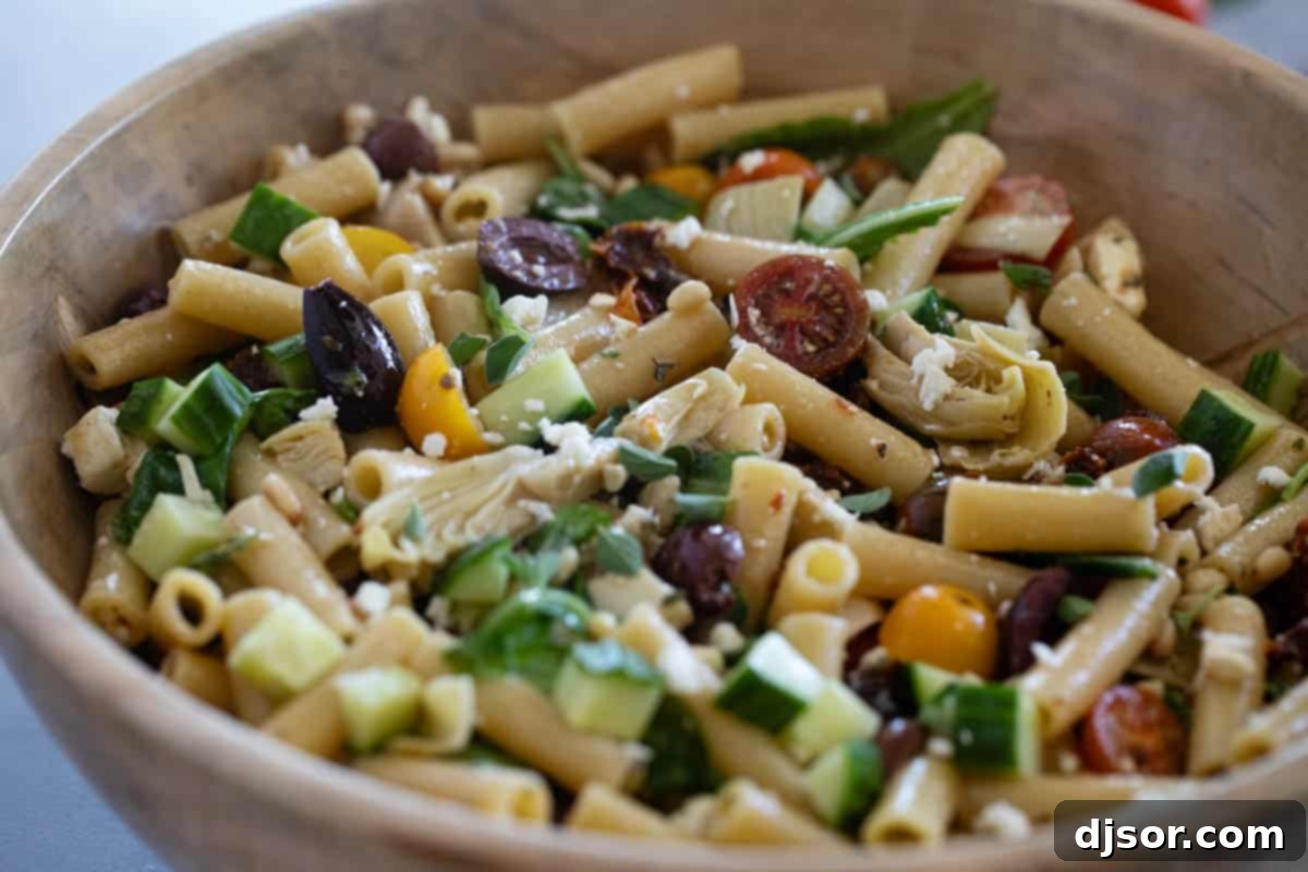 Wooden bowl filled with Mediterranean Pasta Salad, showcasing pasta, tomatoes, olives, feta, and fresh herbs.
