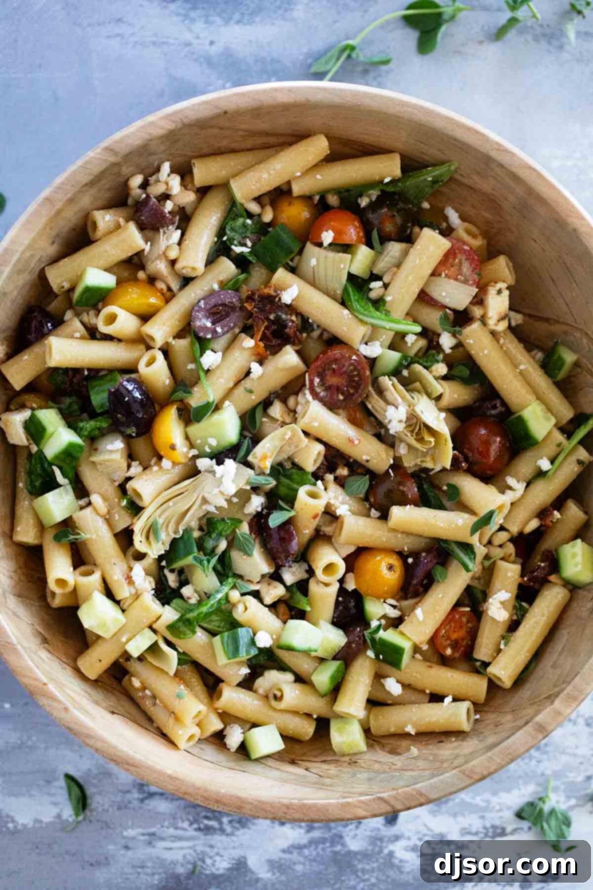 A large wooden bowl showcasing the finished Mediterranean Pasta Salad, brimming with colorful pasta, olives, feta, and fresh vegetables.
