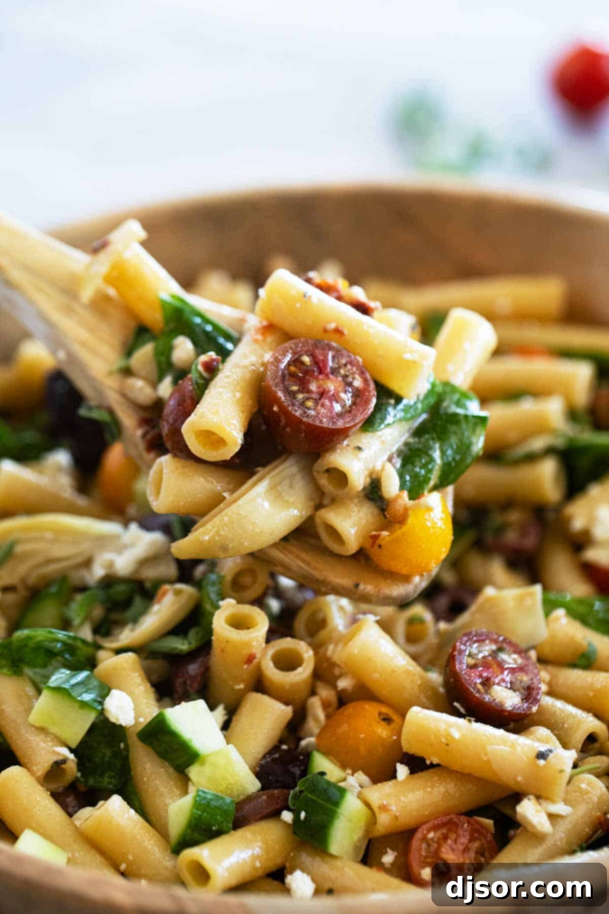 A wooden spoon scooping a portion of Mediterranean Pasta Salad, highlighting the fresh, colorful ingredients.