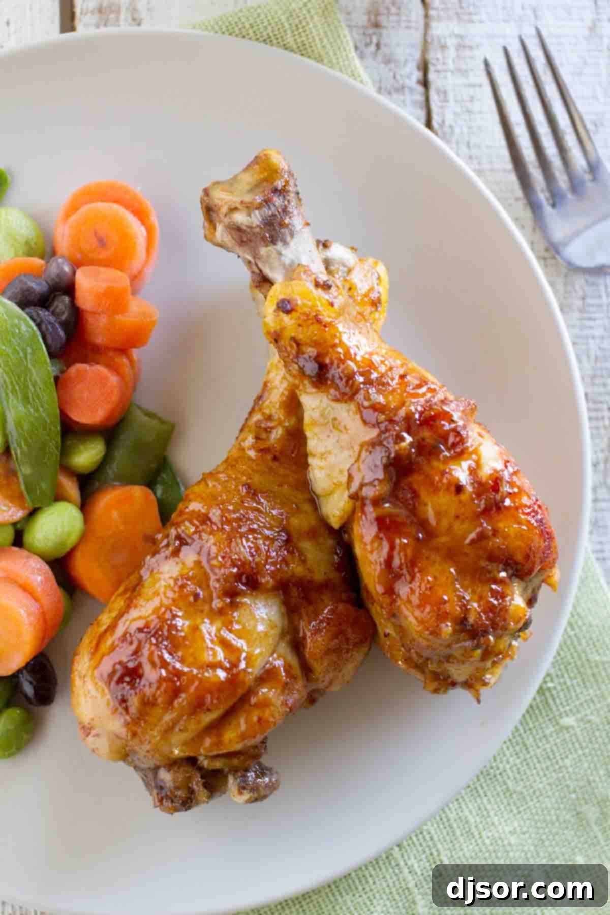 Sticky and sweet, these Honey Balsamic Drumsticks will be a meal that the whole family will devour! Plus a review of 400 Calories or Less with Our Best Bites. Close-up shot of two Honey Balsamic Chicken Drumsticks, glistening with sweet and savory sauce, on a white plate, showcasing their perfect char.