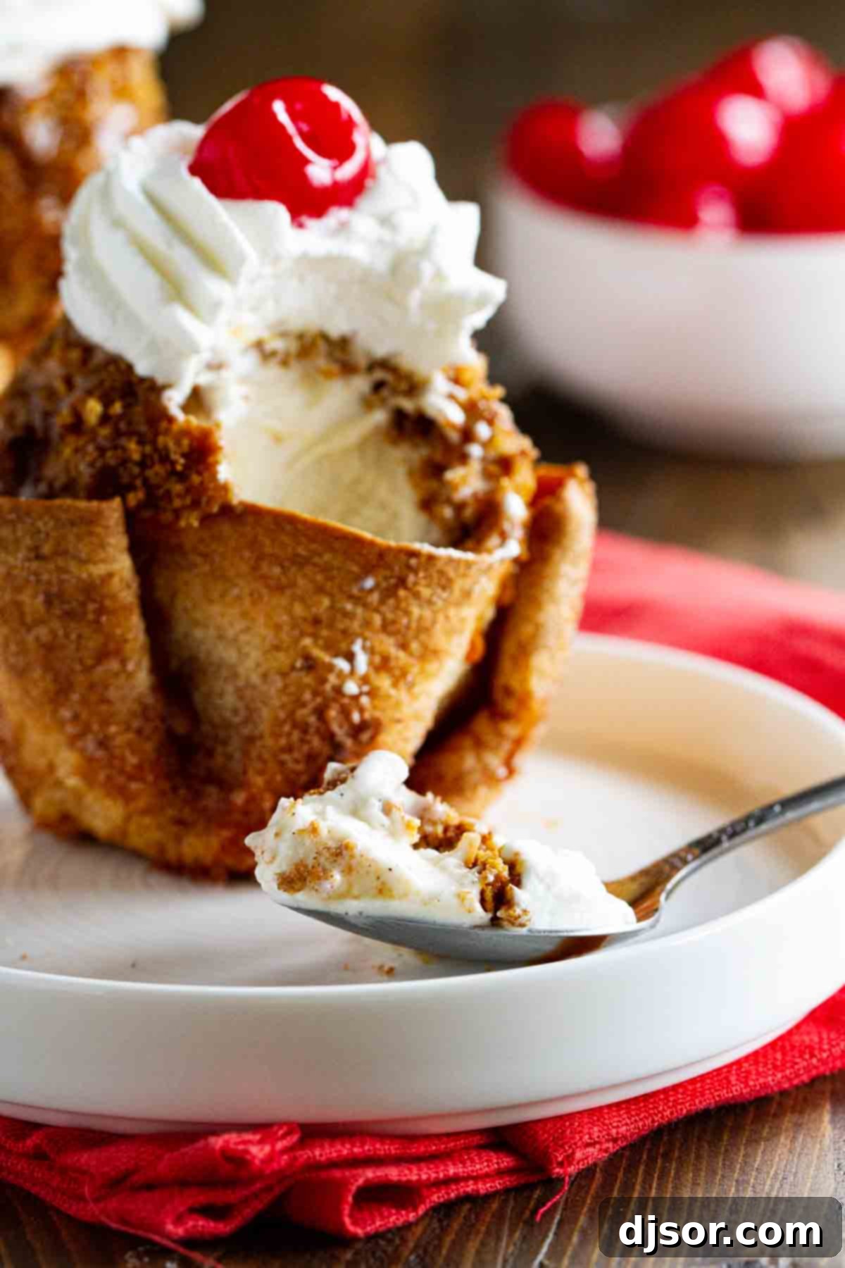 Close-up of fried ice cream in a cinnamon sugar tortilla bowl, with a spoonful showing the crispy crust and creamy interior, garnished with whipped cream and a cherry.