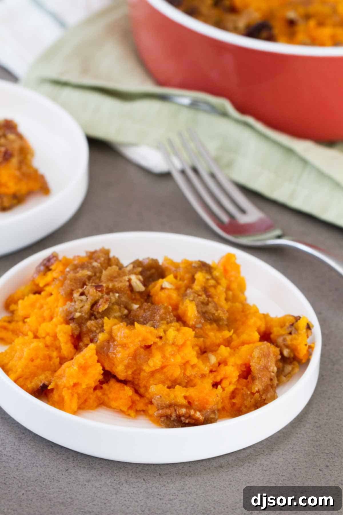 A plate of delicious sweet potato casserole A serving of sweet potato casserole on a white plate with a fork, showing the creamy filling and crunchy streusel topping.