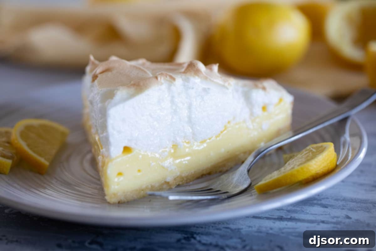 A perfectly sliced French Lemon Cream Tart with Meringue on a white plate, showcasing its golden crust, pale yellow filling, and fluffy toasted meringue.