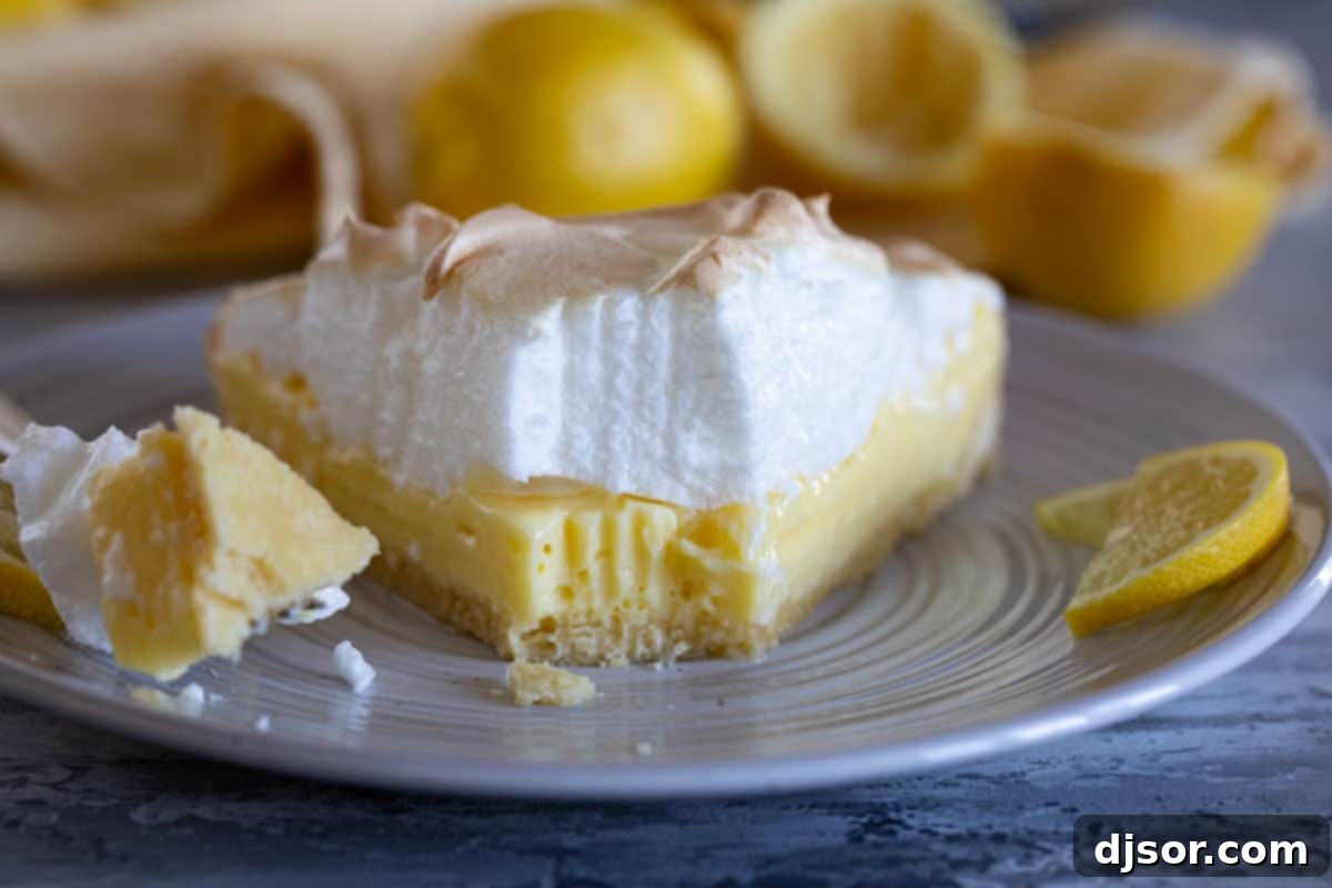 A close-up of a slice of lemon cream tart with meringue, showing a bite taken, revealing the textures of the crust, filling, and meringue.