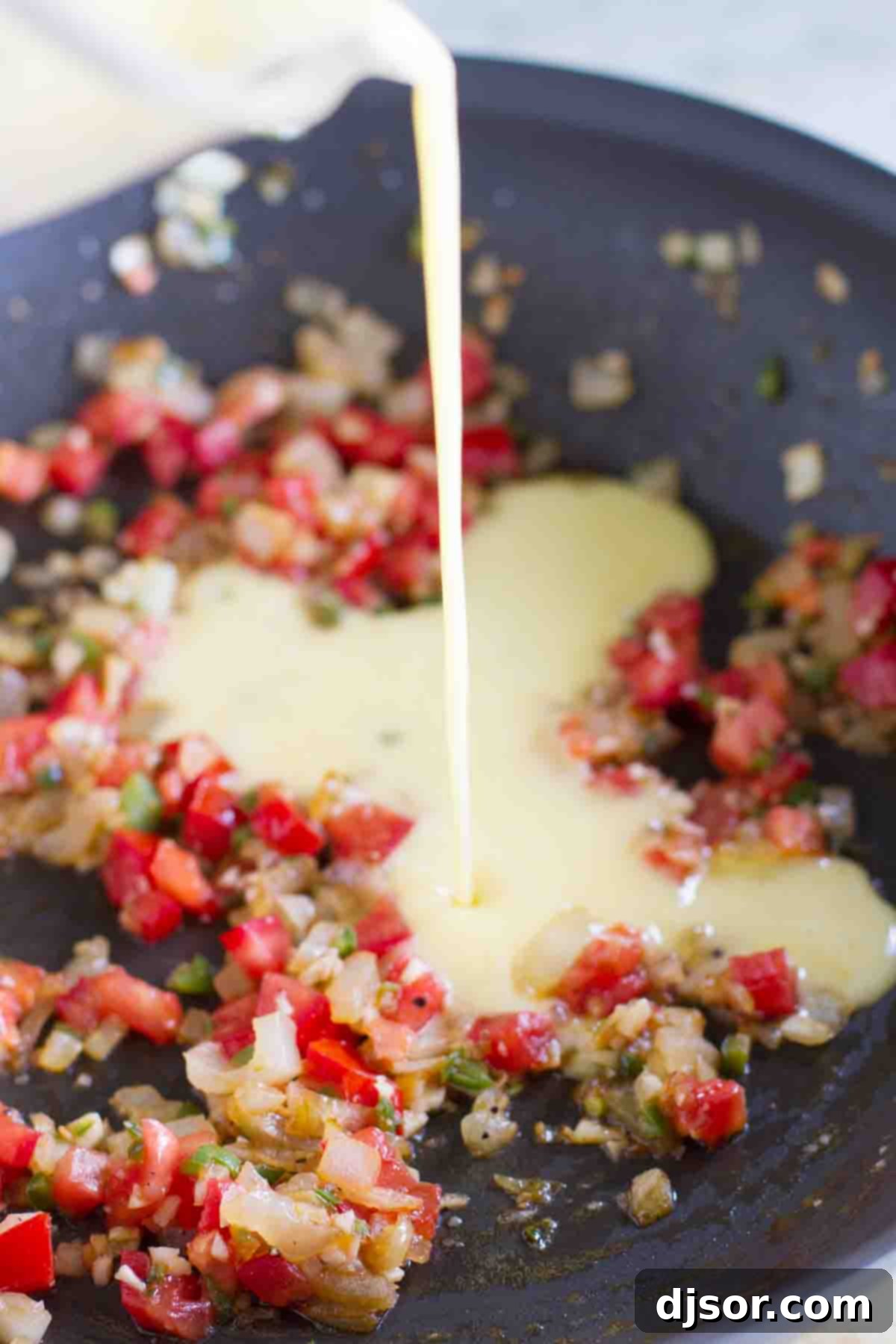 Cooking Migas: Eggs Meeting Sautéed Vegetables Scrambled eggs being poured into a skillet with sauteed tomatoes, onions, and jalapeños