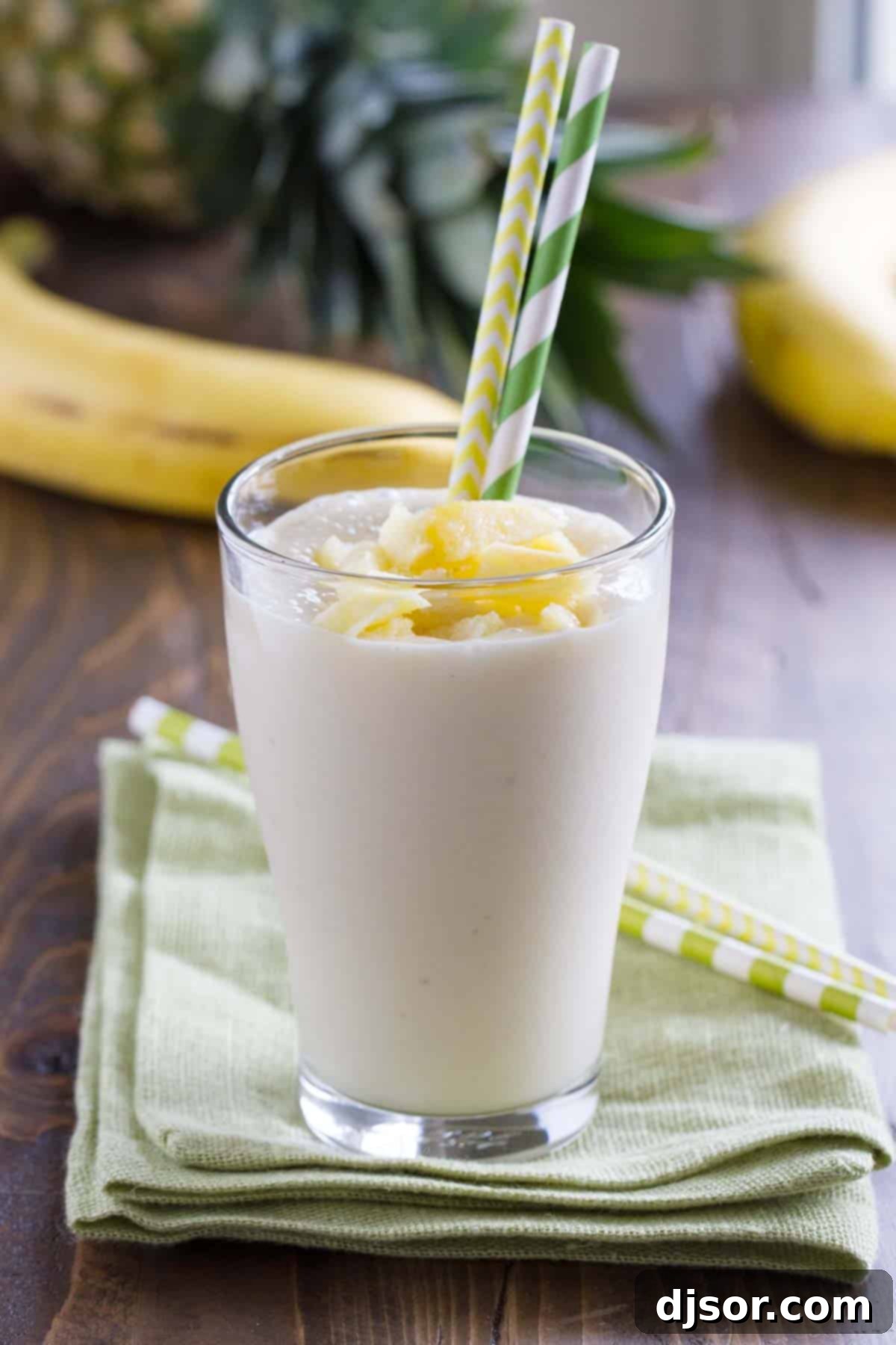 Pineapple Banana Smoothie served in a tall glass with two colorful straws, ready to be enjoyed as a refreshing and healthy drink. Ideal for breakfast, a snack, or post-workout.