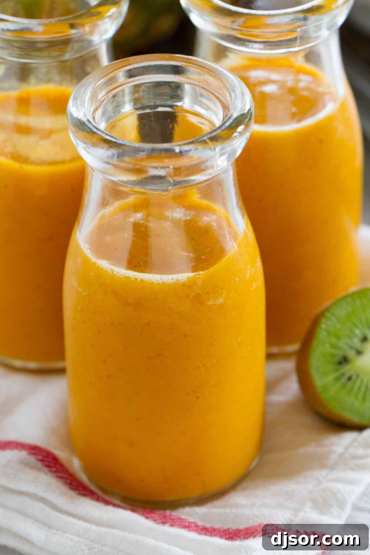 Golden Tropics Carrot Sip 3 Close-up of a single glass of refreshing tropical carrot smoothie, highlighting its smooth texture and rich, orange color, with tropical fruit in the background.
