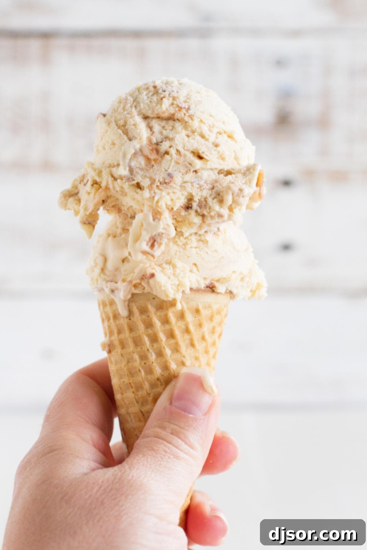 A close-up of a sugar cone filled with homemade salted caramel ice cream, showcasing the rich caramel color, fudge swirls, and generous pieces of toasted coconut.