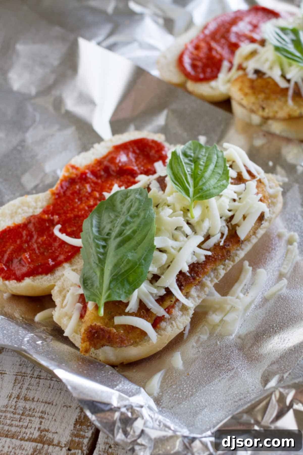 Baked Chicken Parmesan Sandwiches with a hoagie roll, marinara sauce, chicken parmesan, melted cheese, and fresh basil, all assembled in a foil packet before baking.