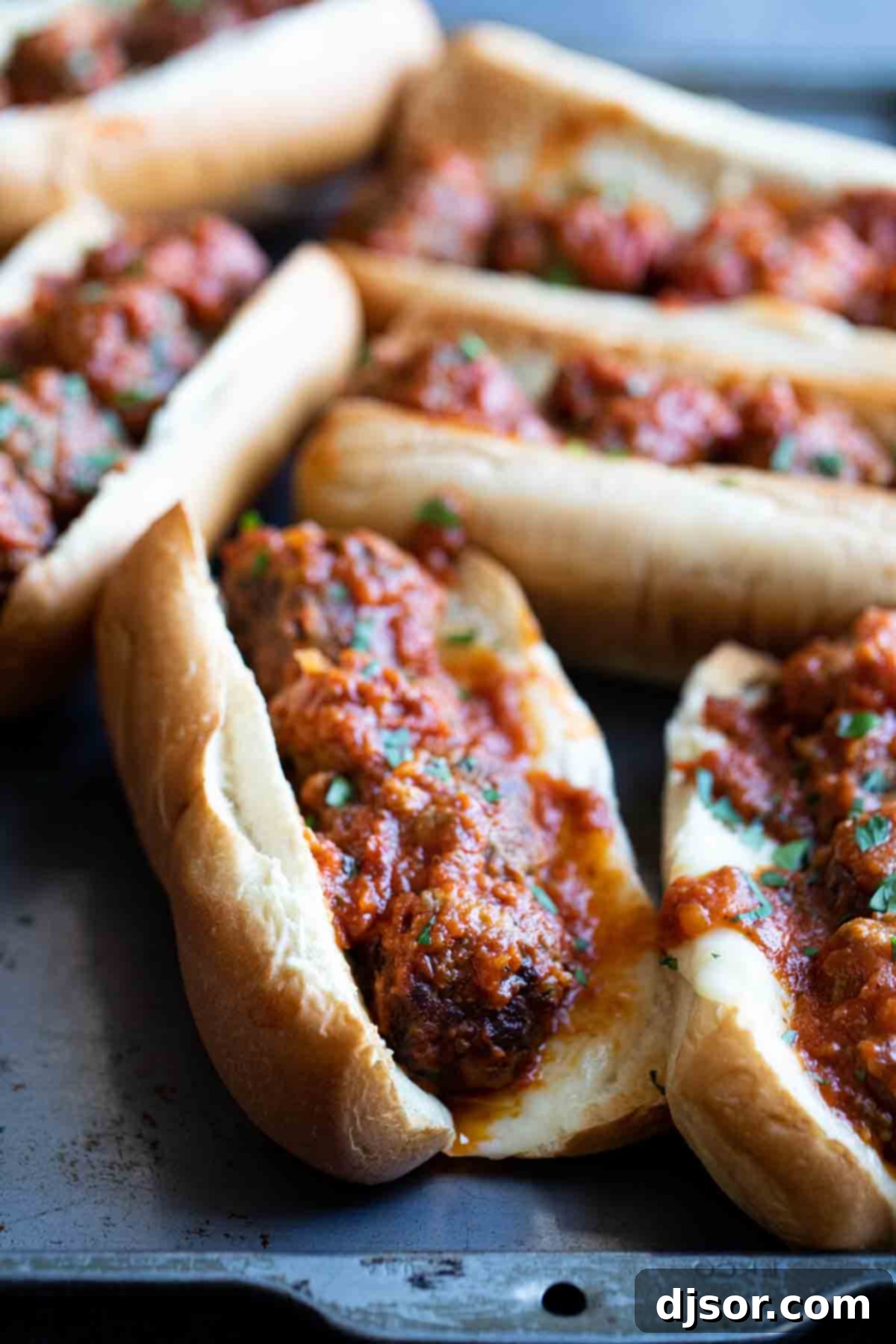 Tray of Irresistible Homemade Meatball Subs Several piping hot homemade meatball subs arranged on a tray, garnished with fresh parsley and overflowing with sauce and melted cheese.