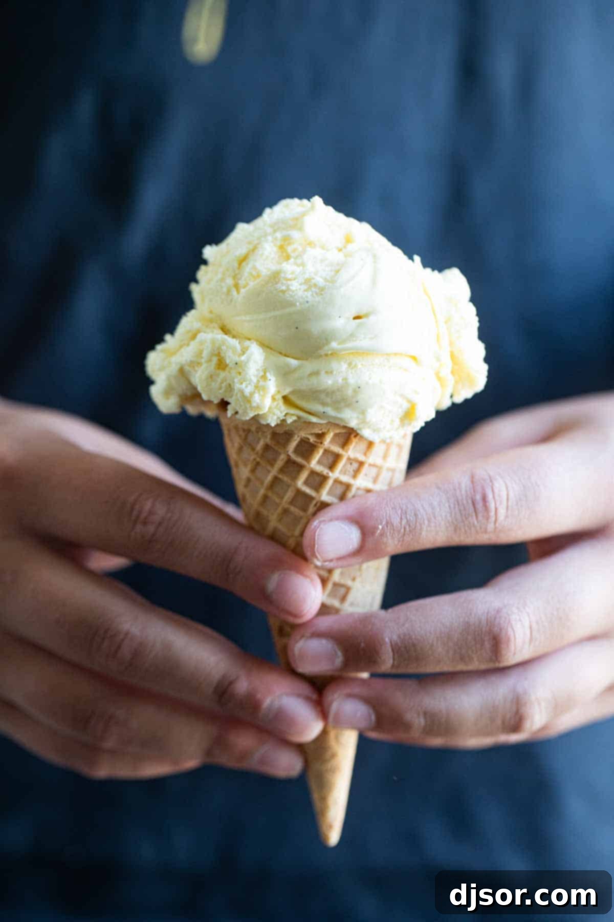 Hands holding a scoop of vanilla ice cream in a sugar cone