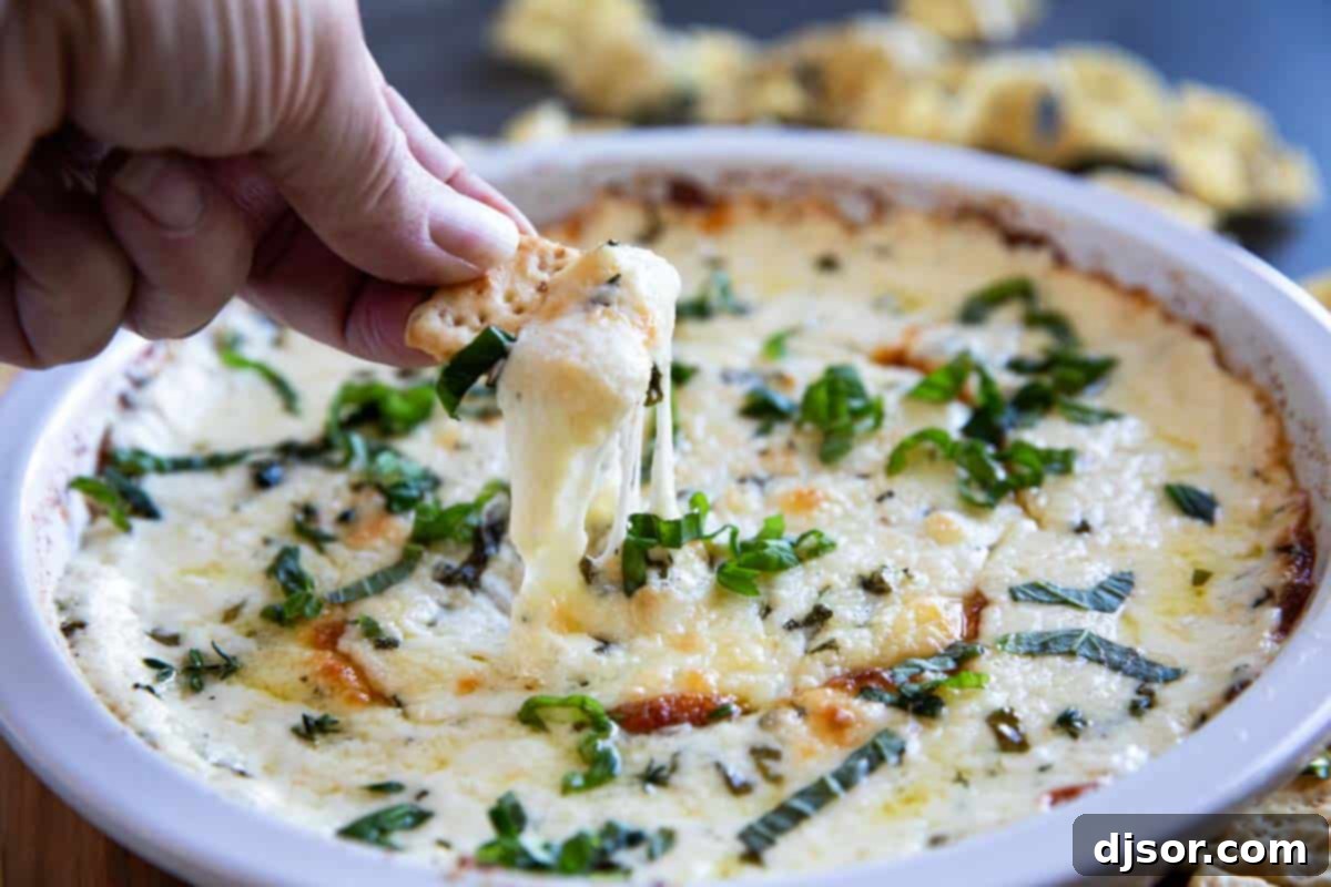 Creamy White Cheese Dip 2 White cheese dip in a dish with a cracker pulling some of the dip out showing cheese pull.