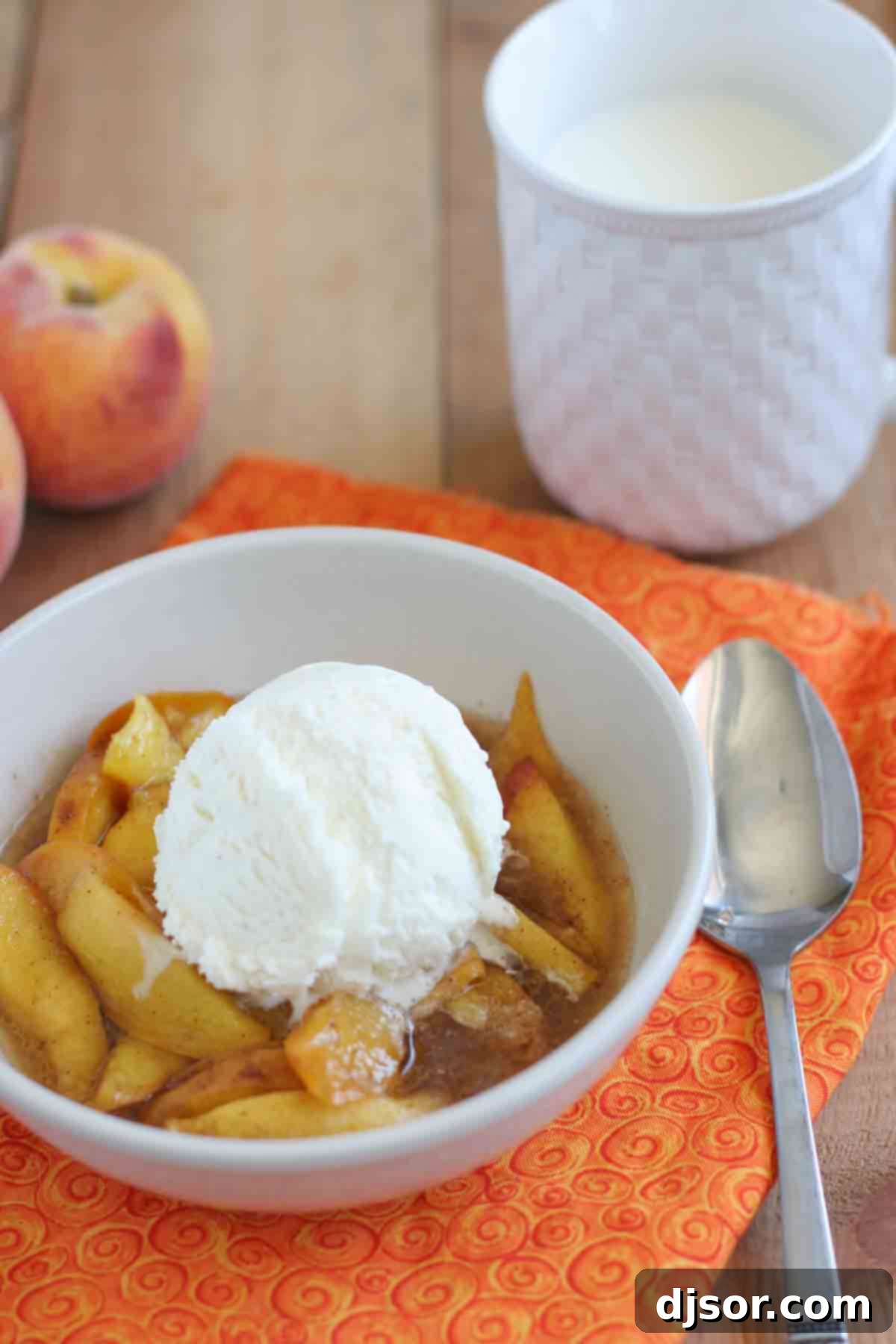 A beautiful close-up of warm slow-cooked peaches in a bowl, generously topped with a scoop of melting vanilla ice cream, creating a creamy and sweet dessert.