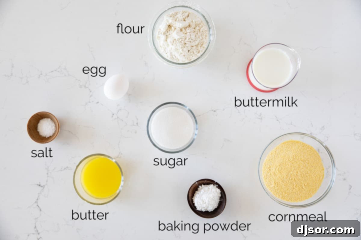 A beautifully arranged spread of fresh, raw ingredients on a kitchen counter, showcasing all the components needed to prepare a delicious homemade cornbread. These include measured flour, vibrant yellow cornmeal, granulated sugar, baking powder, salt, a bowl of buttermilk, a small dish of melted butter, and a single fresh egg, all perfectly staged for baking.