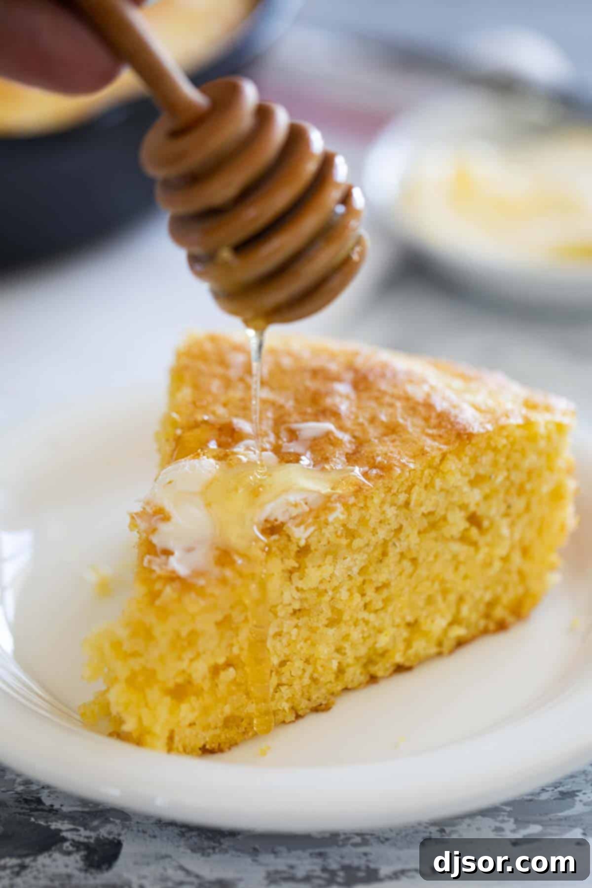 A tantalizing close-up shot of rich, golden honey being drizzled generously over a warm, freshly sliced piece of cornbread, highlighting its moist texture and inviting sweetness.