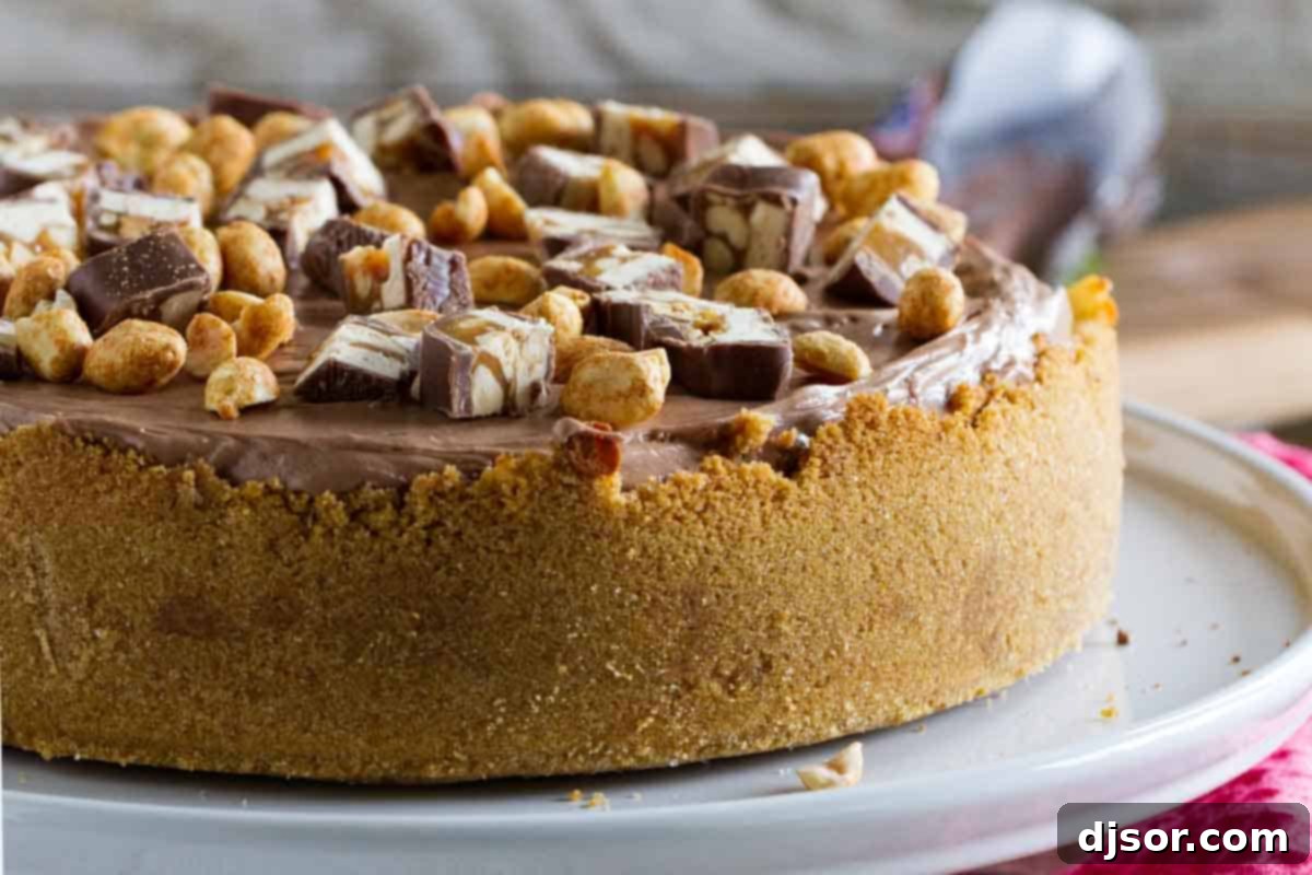 A stunning full Snickers cheesecake displayed on a serving platter, beautifully frosted and garnished with chopped Snickers bars and peanuts.