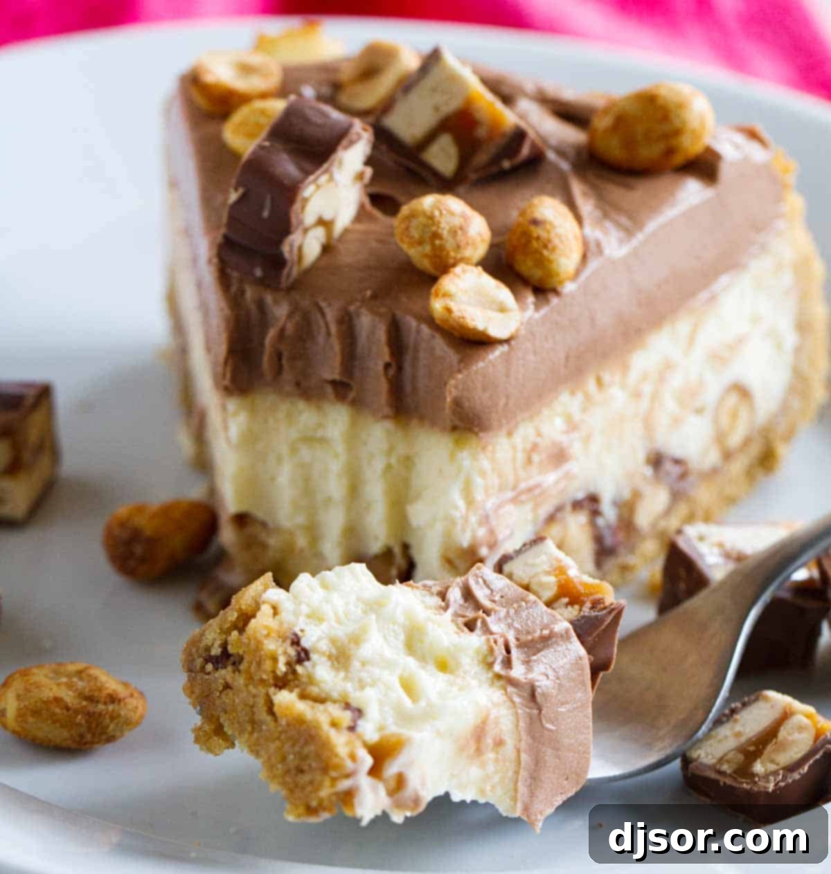 A close-up of a fork taking a bite from a slice of Snickers cheesecake, highlighting the textures and layers.