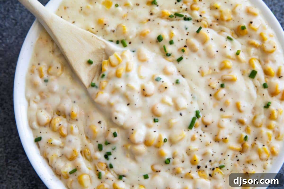 Velvety Sweet Corn 2 A bowl of homemade creamed corn, garnished with fresh herbs and a wooden spoon resting in it, ready to be served.