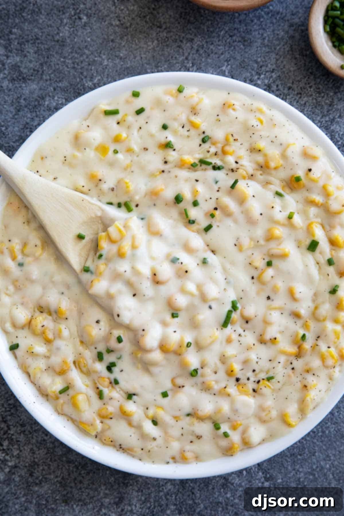 Velvety Sweet Corn 6 A beautifully presented bowl of creamy, homemade creamed corn, generously topped with freshly cracked black pepper and chopped chives, ready for serving.