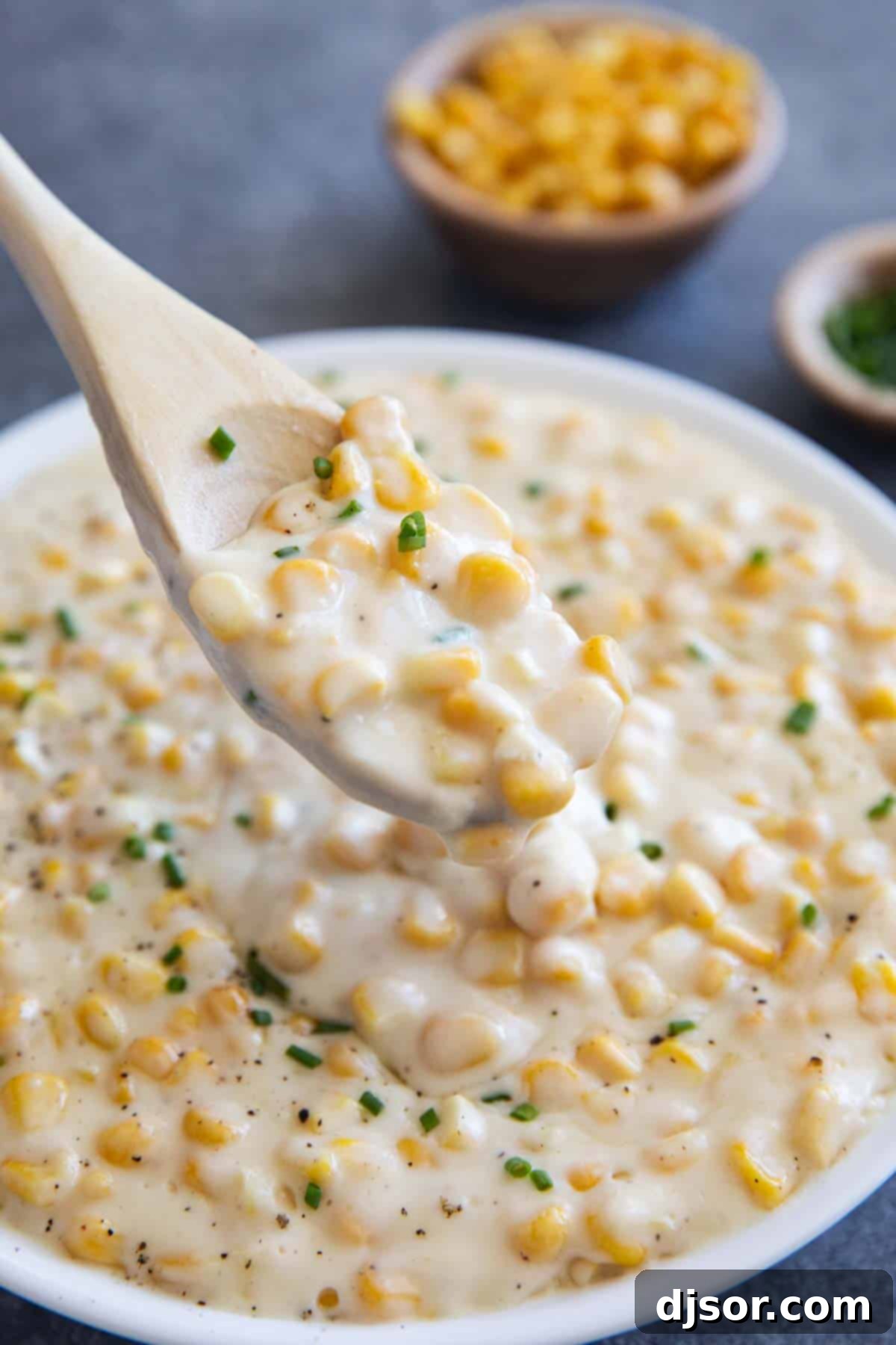 Velvet Corn Bliss 6 Wooden spoon scooping out creamed corn topped with chives.