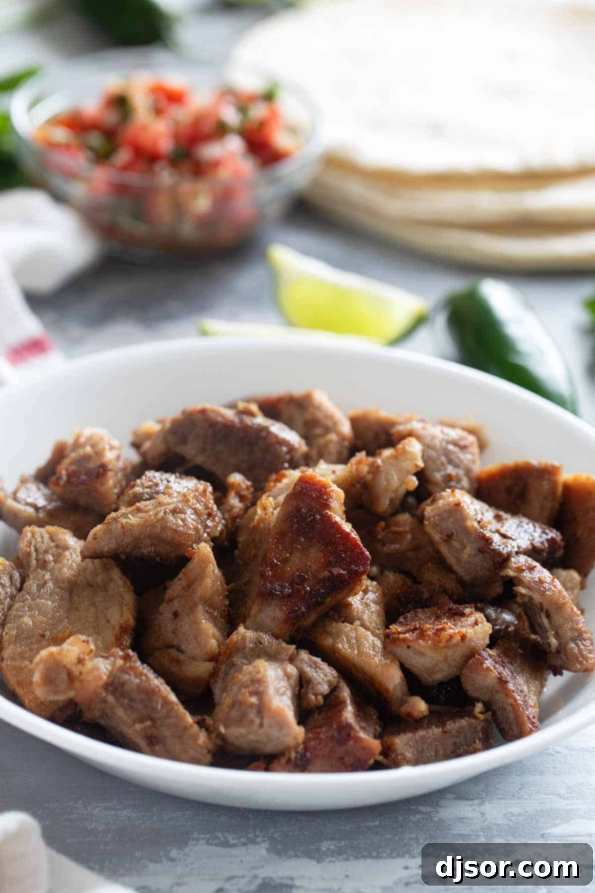 Slow-Roasted Crispy Pork Perfection 7 Platter of Pork Carnitas with tortillas, lime wedges, and salsa in the background.