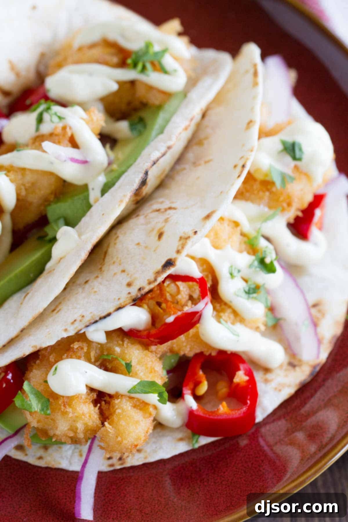 Zesty Crispy Shrimp Tacos 4 Two crispy shrimp tacos on a plate, garnished with vibrant red onions, pickled peppers, and a generous drizzle of homemade mayonnaise, ready to be enjoyed.