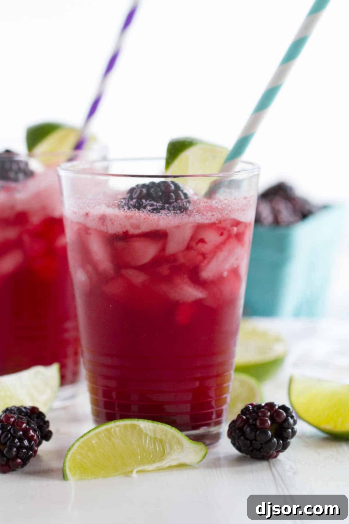 Serve up these delicious Blackberry Lime Sodas Three glasses of blackberry lime soda, each with a straw, garnished with fresh fruit, ready to be served