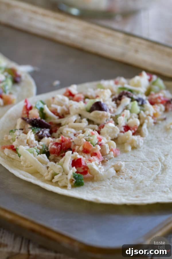 Assembling the Greek Quesadillas: A vibrant mix of fresh ingredients. Fresh Greek quesadilla filling spread on a tortilla before cooking, showing cucumbers, tomatoes, olives, and cheese.