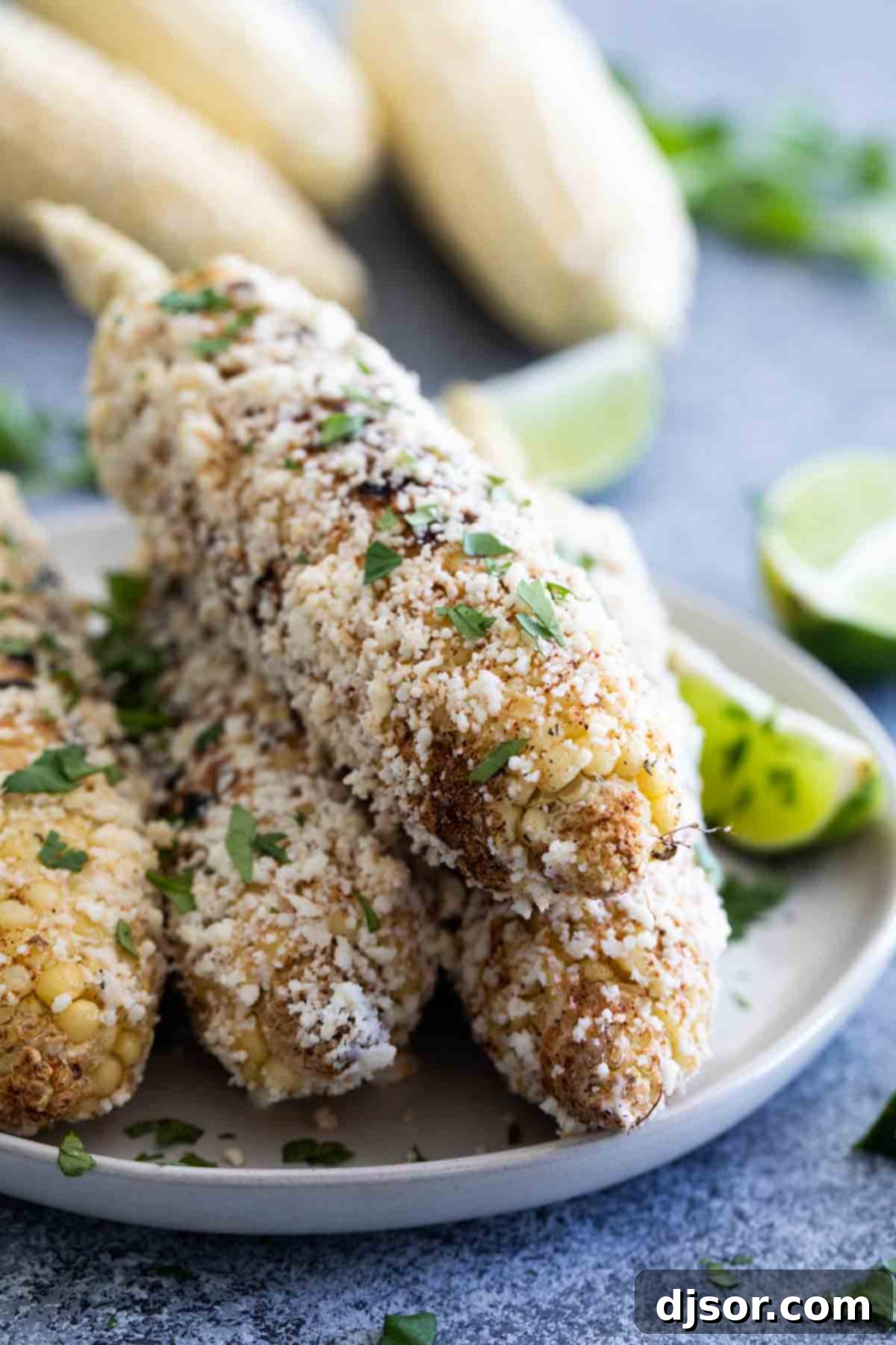 Grilled corn - south of the border style! This Grilled Mexican Corn on the Cob takes grilled corn to the next level with spices, crumbled Cotija cheese, cilantro and fresh squeezed lime. Flavorful Grilled Mexican Corn on the Cob stacked on a rustic wooden platter, adorned with spices, cheese, and fresh lime wedges.