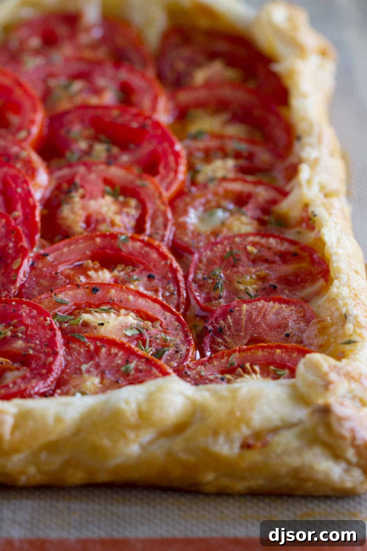 A golden-brown Tomato Tart with Bacon and Gruyere on a flaky puff pastry crust, garnished with fresh herbs, ready to be served.