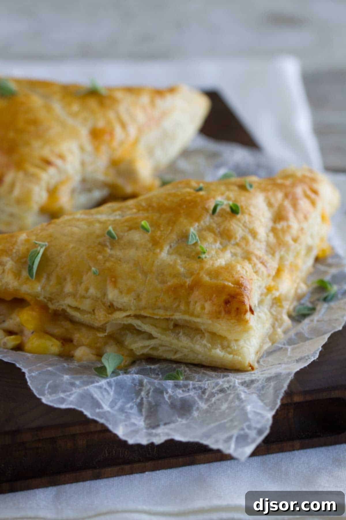 Creamy Chicken and Corn Turnovers - A Family Hit Two golden-brown creamy chicken and corn turnovers on a rustic cutting board, garnished with fresh thyme leaves, showcasing their flaky crust.