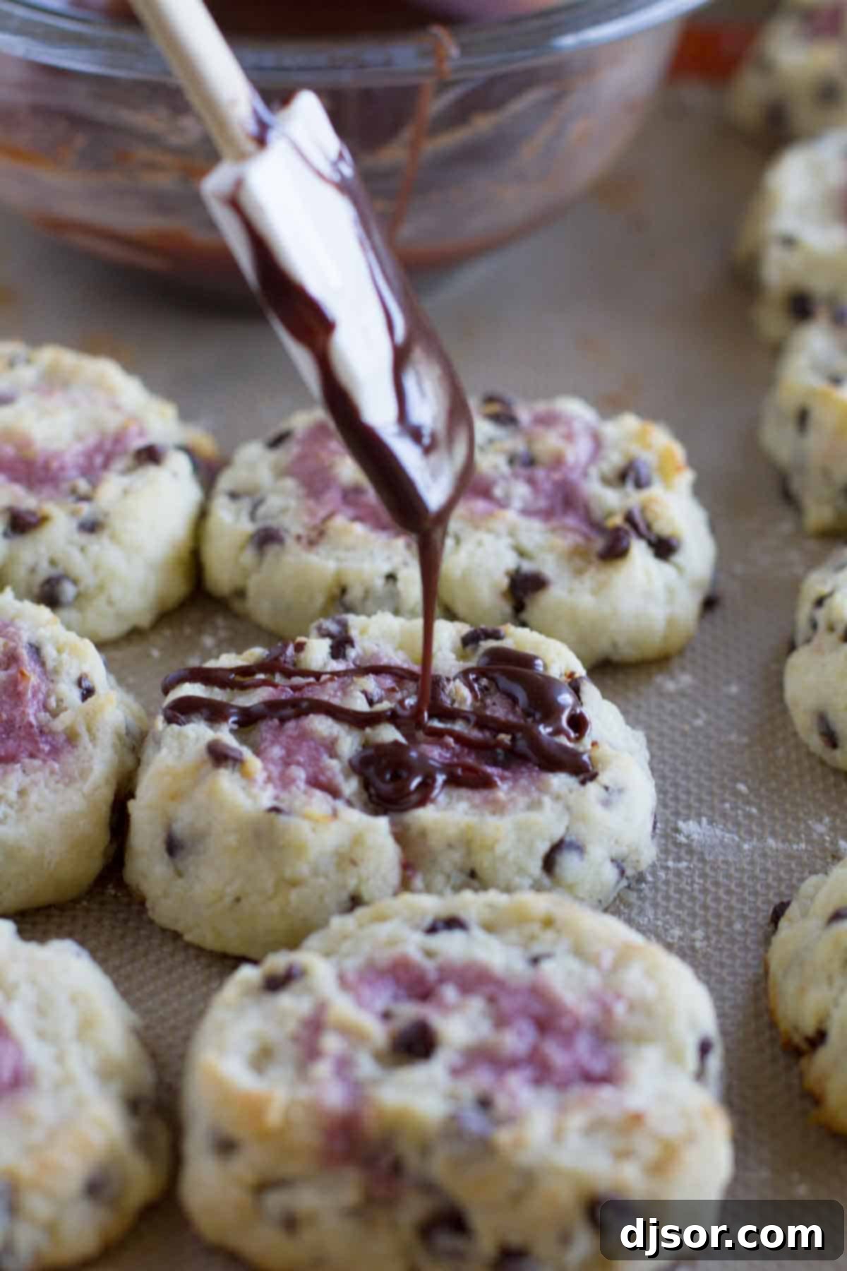 Drizzling rich chocolate glaze over a warm, freshly baked chocolate chip biscuit with raspberry cream