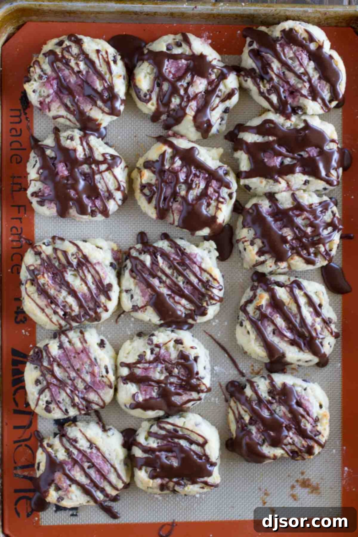Overhead view of a baking sheet filled with golden-brown chocolate chip biscuits with raspberry cream, fresh from the oven