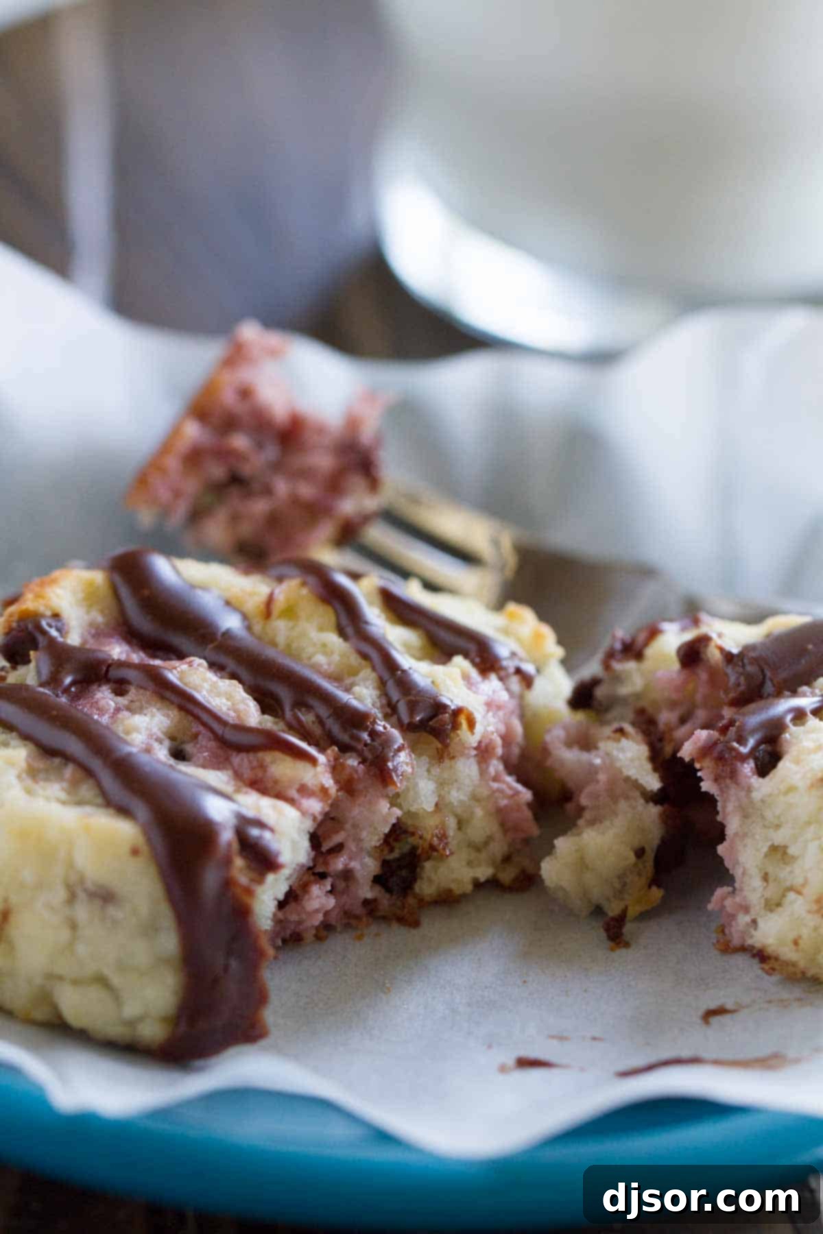 A chocolate chip biscuit with raspberry cream cut in half, revealing the soft interior and fruity filling