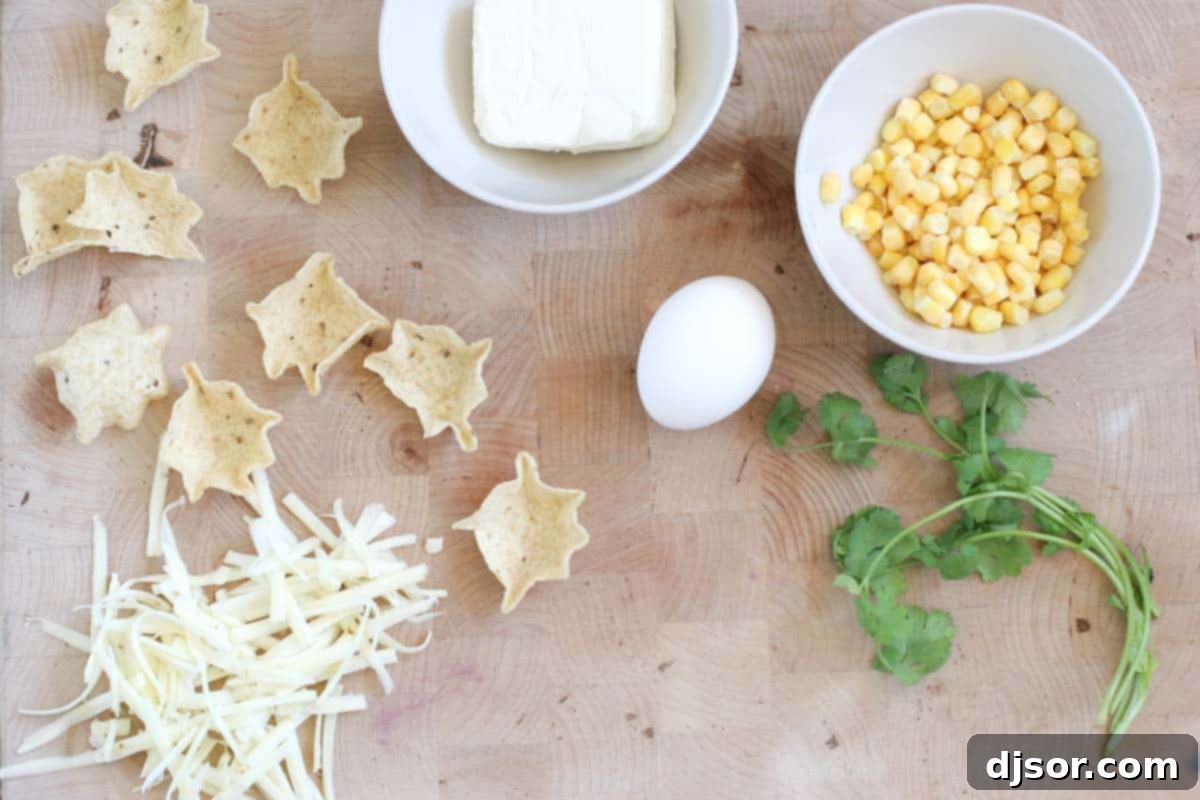 Various ingredients neatly arranged on a kitchen counter, ready to be combined for making Cheesy Corn Bites. Includes cream cheese, shredded pepper jack, a single egg, a bowl of frozen corn kernels, and a package of scoop-shaped tortilla chips.