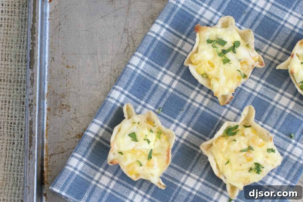 A close-up view of golden-brown Cheesy Corn Bites, sprinkled with fresh cilantro, resting on a textured white towel. Each bite shows a crispy tortilla chip filled with a rich, melted cheese and corn mixture.