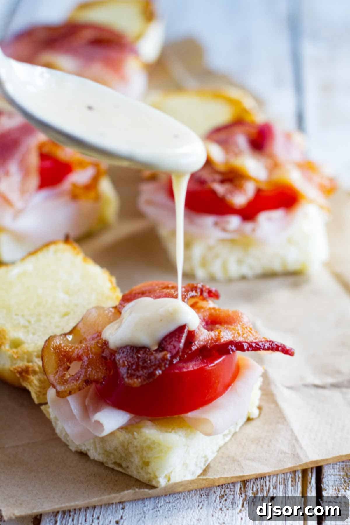 Applying creamy Mornay sauce over easy Kentucky Hot Brown Sliders arranged on a baking sheet.