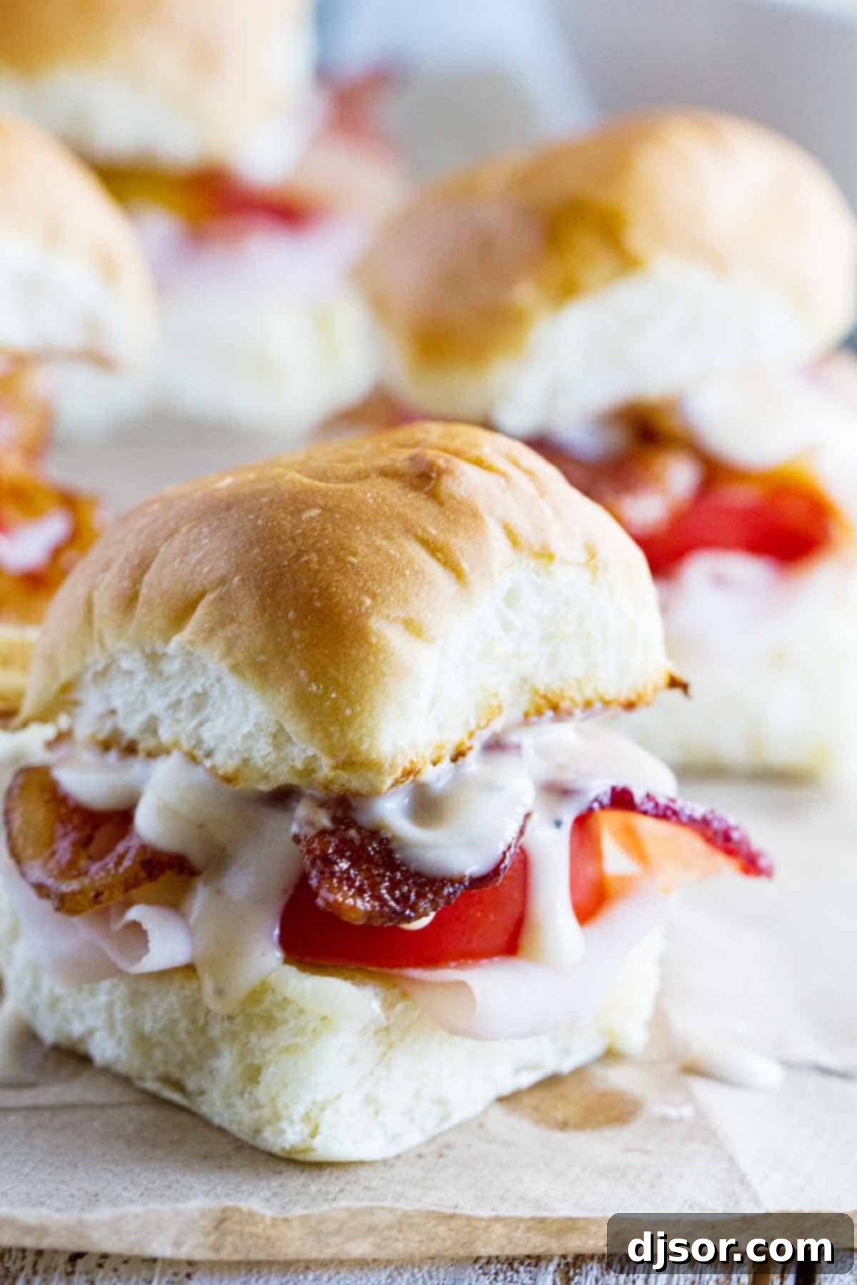A close-up view of two finished Mini Kentucky Hot Brown Sandwiches, showing their golden rolls, generous turkey, bacon, and creamy sauce.