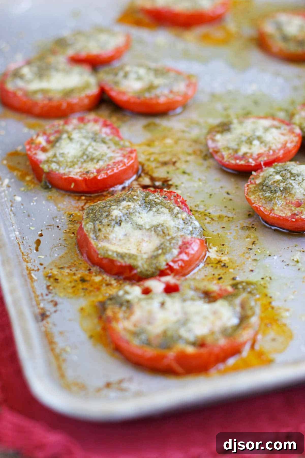 Delicious Roasted Tomatoes with Pesto and Parmesan for a Summer Dish Golden-brown roasted tomato slices, generously topped with vibrant green pesto and melted, bubbly Parmesan cheese on a parchment-lined baking sheet.