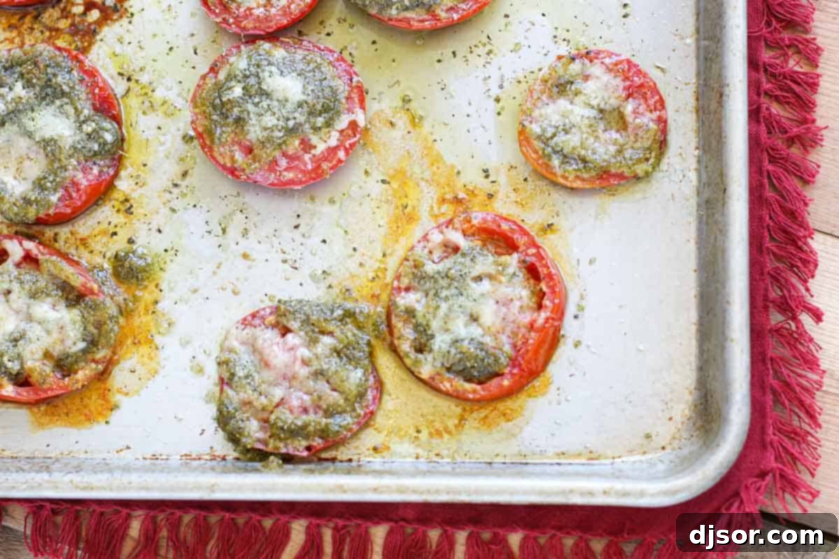 Pesto and Parmesan Topped Roasted Tomatoes Ready to Serve A close-up view of roasted tomato slices layered with vibrant basil pesto and a golden crust of melted Parmesan cheese in a baking dish, glistening and hot from the oven.