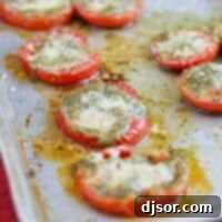Oven Roasted Pesto Tomatoes 2 A small round image of roasted tomatoes topped with pesto and Parmesan on a baking sheet, ready for serving.