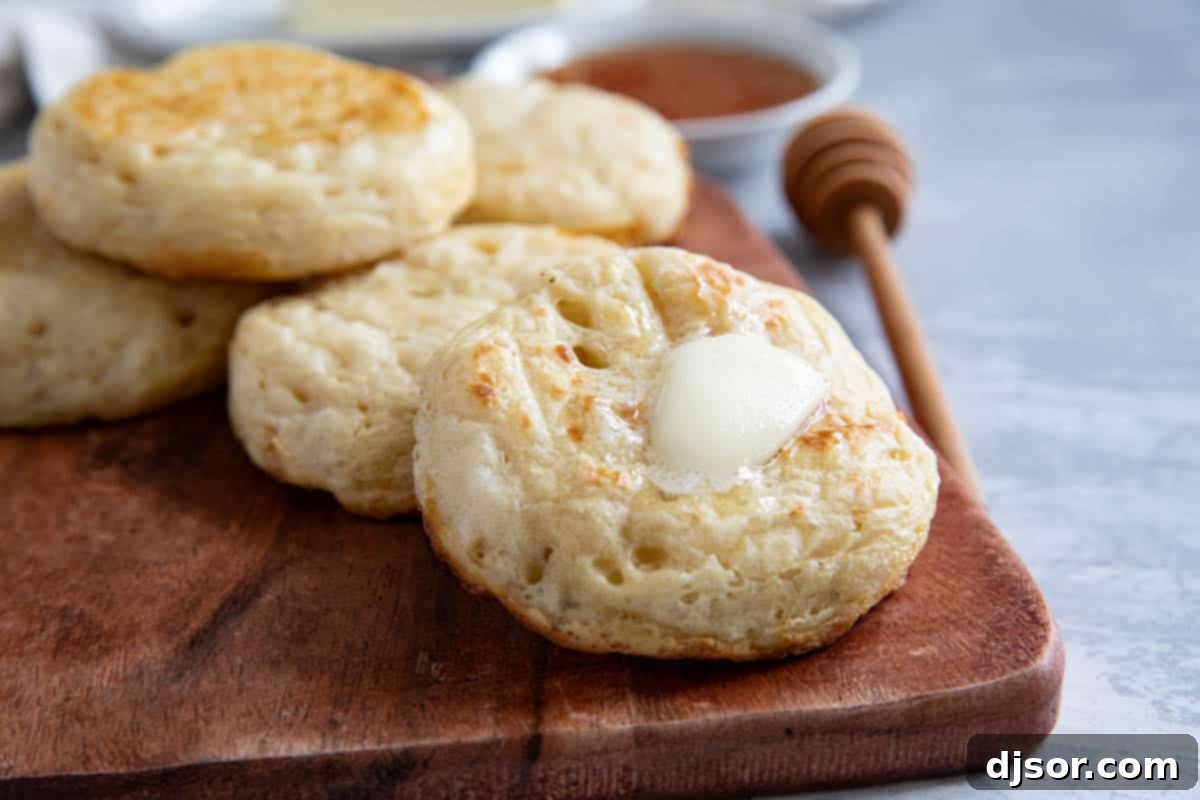 Freshly cooked crumpets on a cutting board, with one topped with melting butter.