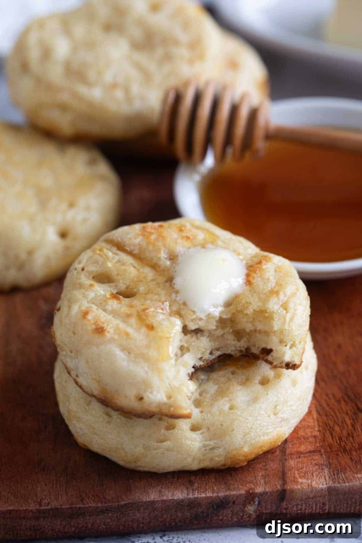 A stack of golden-brown crumpets with a pat of butter melting on the top crumpet.