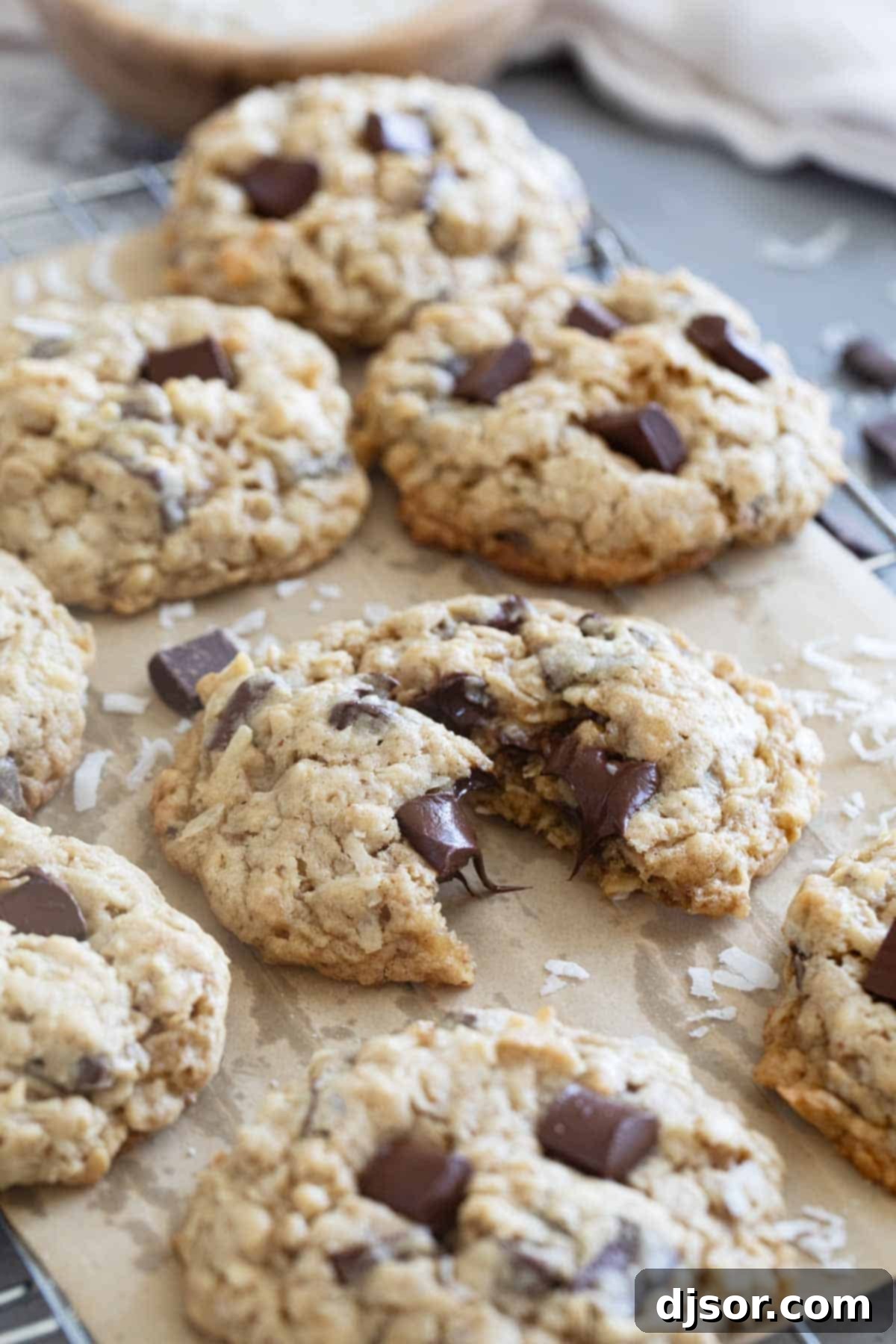 Freshly baked Chocolate Chunk Oatmeal Coconut Cookies on a cooling rack, with one cookie broken in half to reveal its chewy interior and melted chocolate.